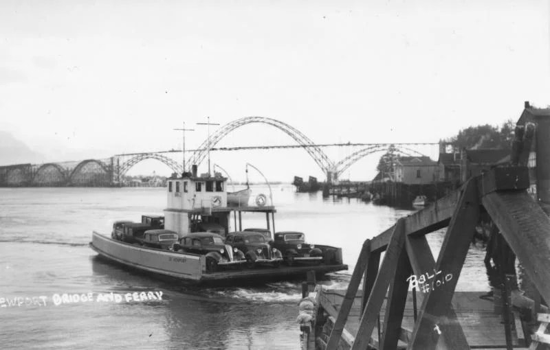 Vintage photo of a ferry carrying cars with a bridge in the background.