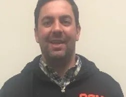 A smiling man in a black jacket with a blurred background.