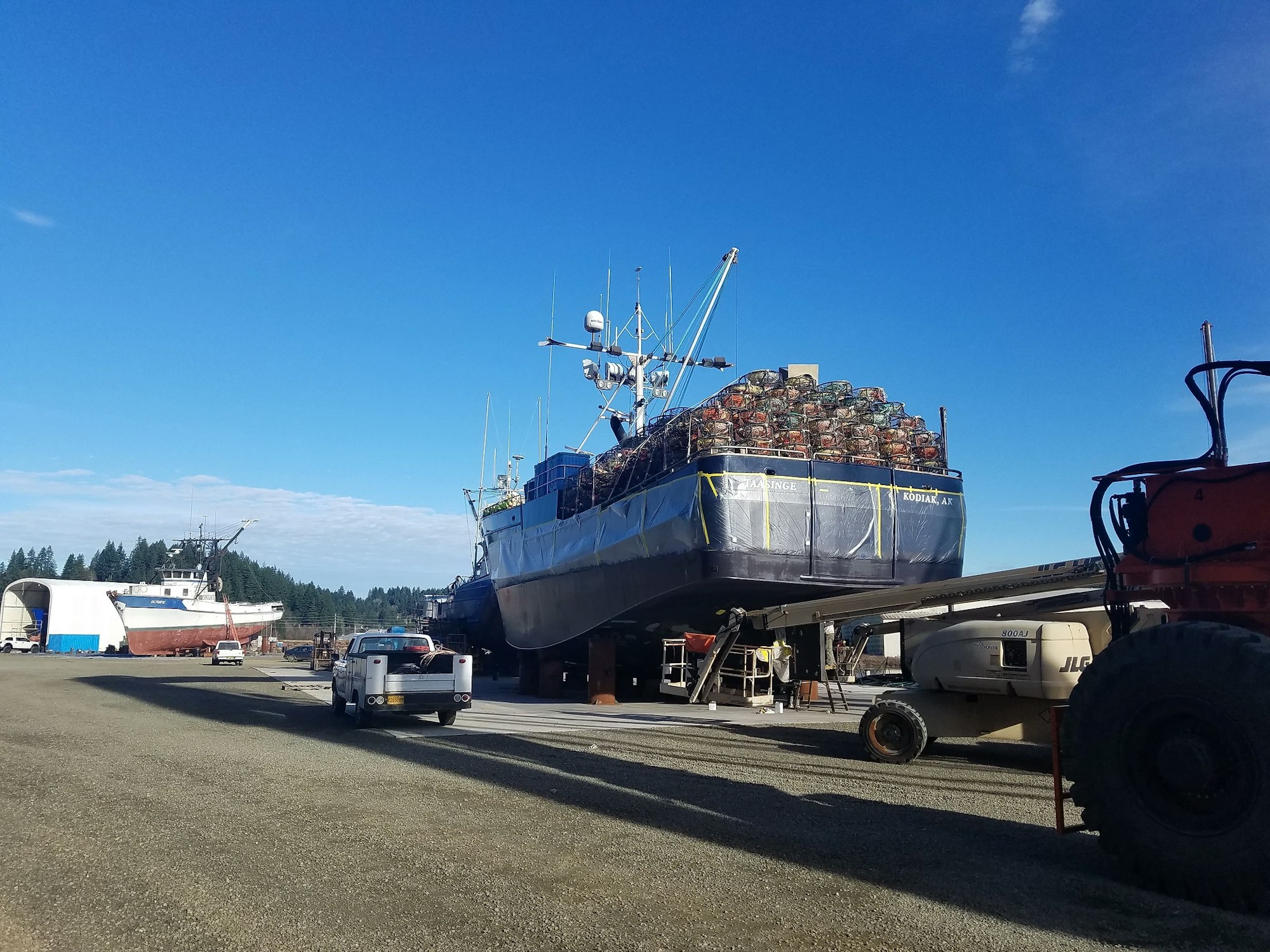 A fishing boat loaded with crab pots in a dry dock on a sunny day, with clear blue sky.