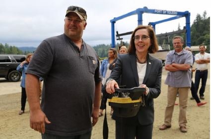 Two people holding a helmet outdoors, with onlookers in the background.