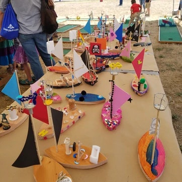 Handcrafted model boats displayed on a table, some embellished with colorful sails and decorations.