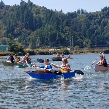 People kayaking on a sunny day, with trees and hills in the background.
