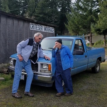Two people leaning on a blue pickup truck, smiling, with a building labeled "CRITZER MORAGE" in the background.