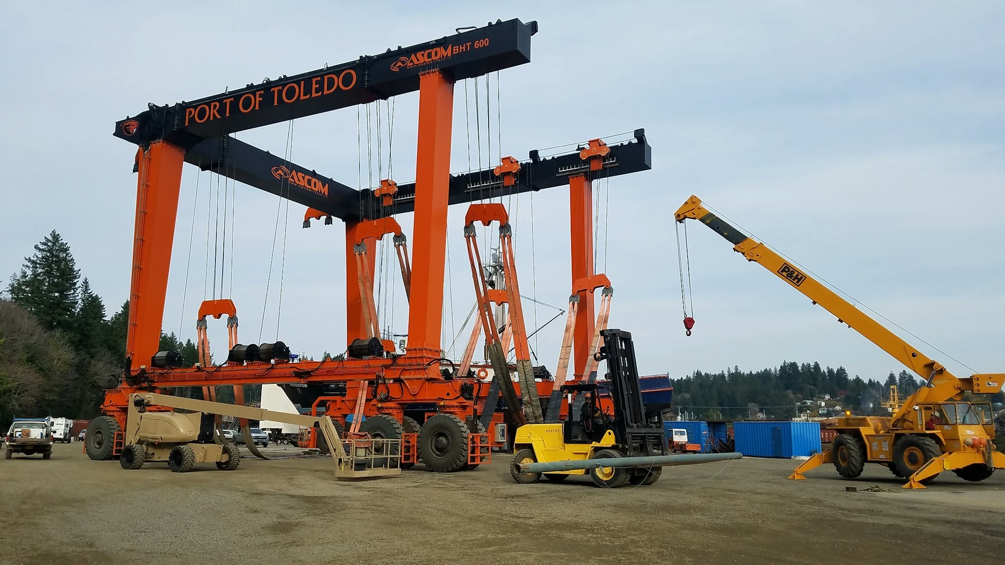 A heavy-duty orange gantry crane at Port of Toledo, industrial vehicles, and construction equipment on a clear day.