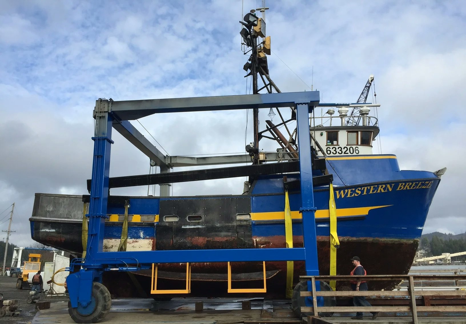 A boat named "Western Breeze" on dry dock for maintenance or repairs, with a person walking by.