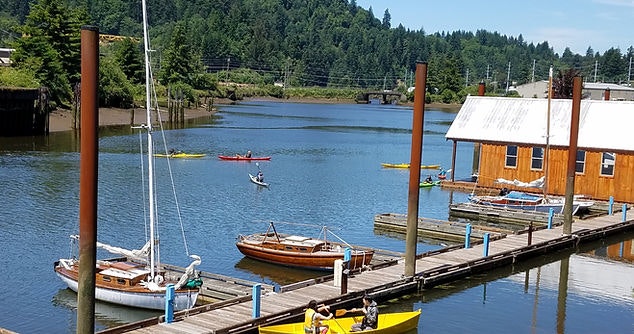 A river with kayaks, docked boats, and a boathouse under a clear blue sky.