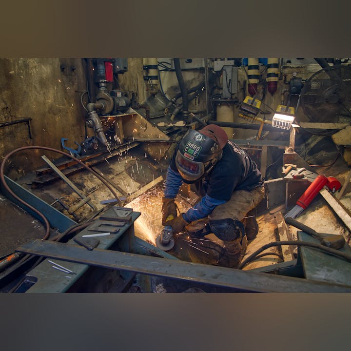 A welder is grinding metal, with sparks flying around in a workshop setting.