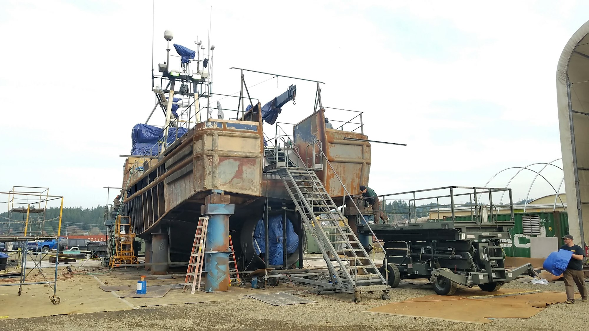 A large ship undergoing repairs or maintenance in a dry dock with workers and equipment around.