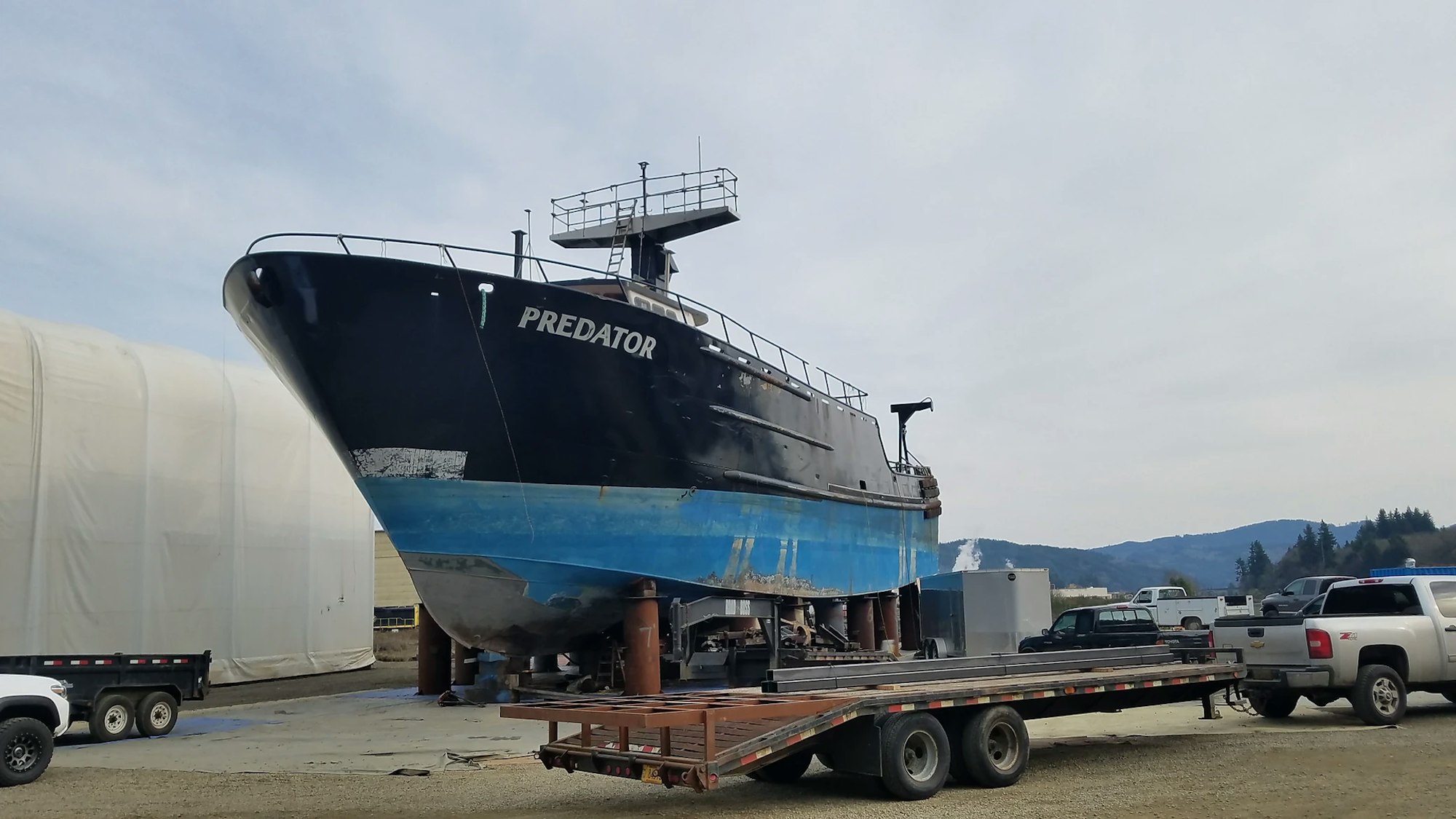 A large boat named PREDATOR on dry land, supported by beams and blocks, with vehicles parked nearby.