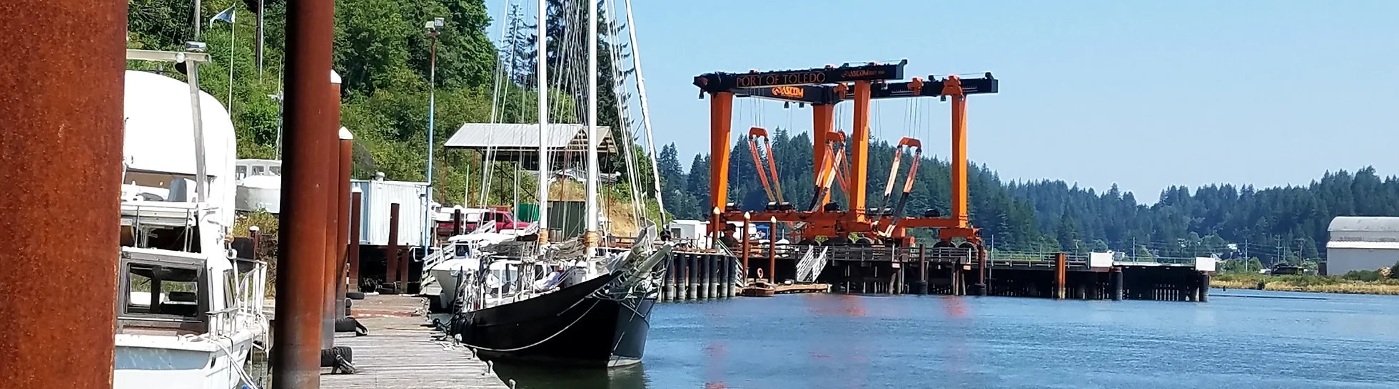 Marina with boats and a large orange boat lift labeled "Port of Toledo." Sunny day with clear skies.