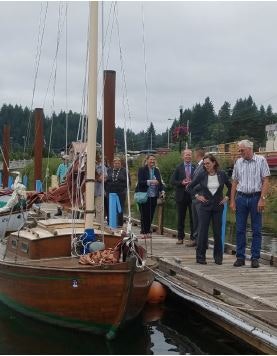 People on a dock looking at a wooden sailing boat.