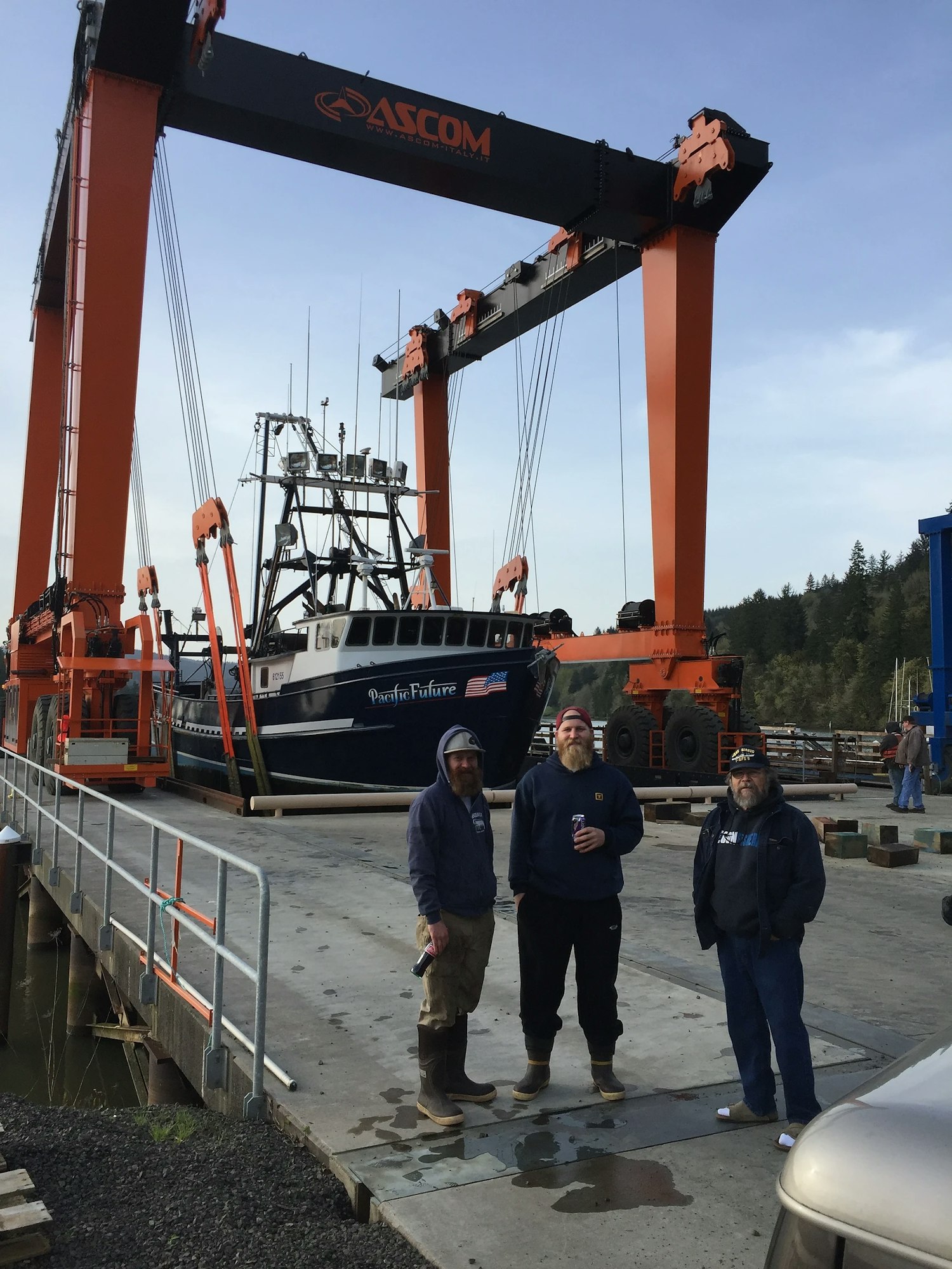 Three men in work gear with a boat and a large crane at a dockyard.
