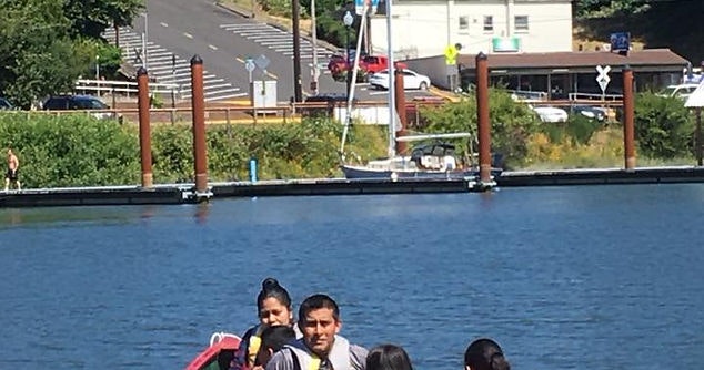 People by a dock, a boat in the background, and clear blue skies.
