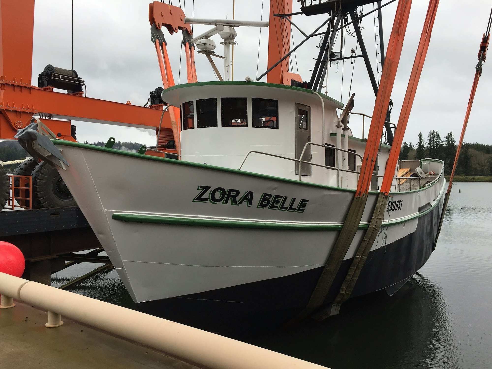 A fishing boat named "ZORA BELLE" is docked with booms and rigging visible against a cloudy sky.
