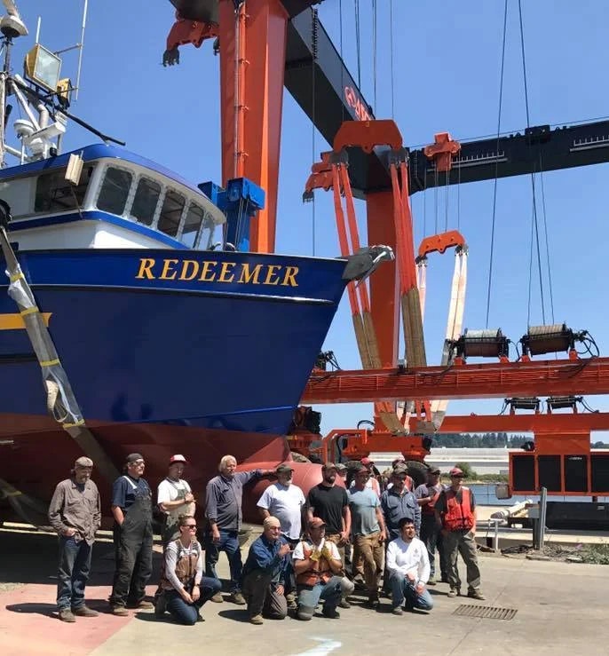 Group of people in front of a boat named "REDEEMER" with a travel lift.