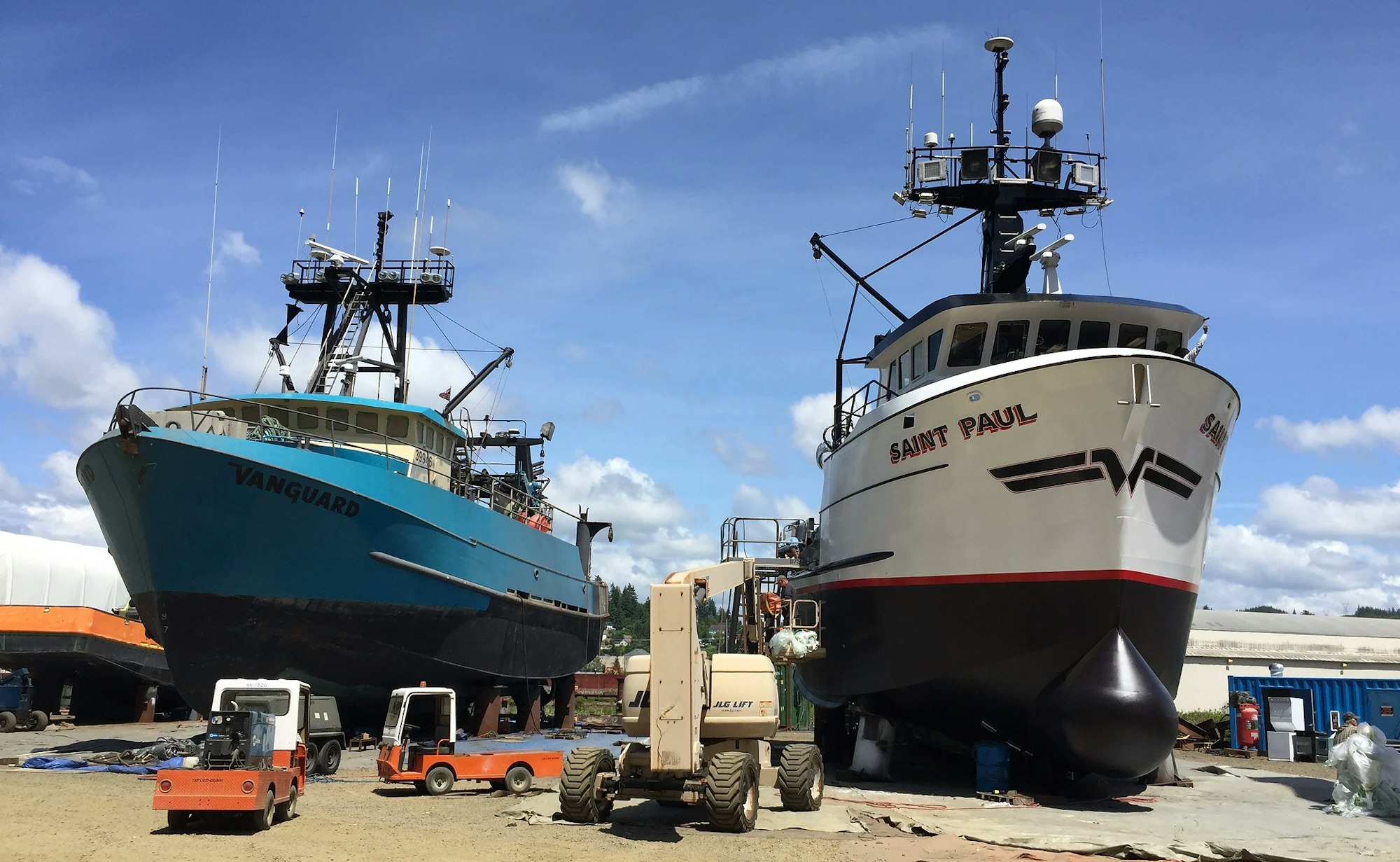 Two large fishing boats, "Vanguard" and "Saint Paul," in a dry dock for repairs or maintenance, under a blue sky with clouds.
