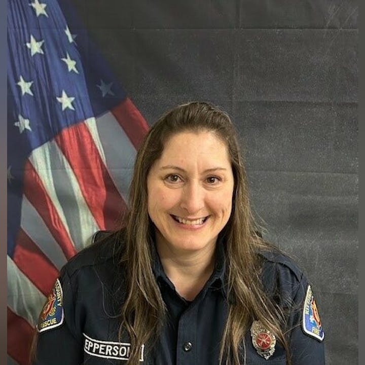 Smiling person in a uniform, standing in front of a U.S. flag backdrop.