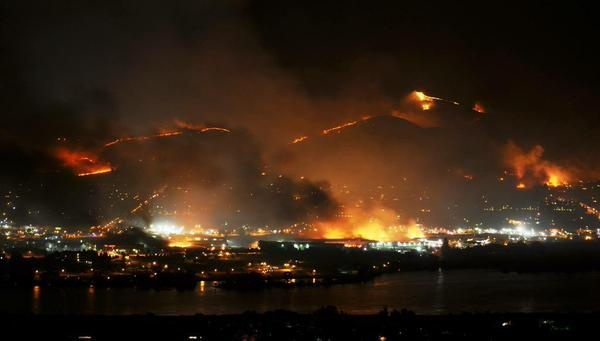 A night landscape with wildfires on hills and a city in the foreground.