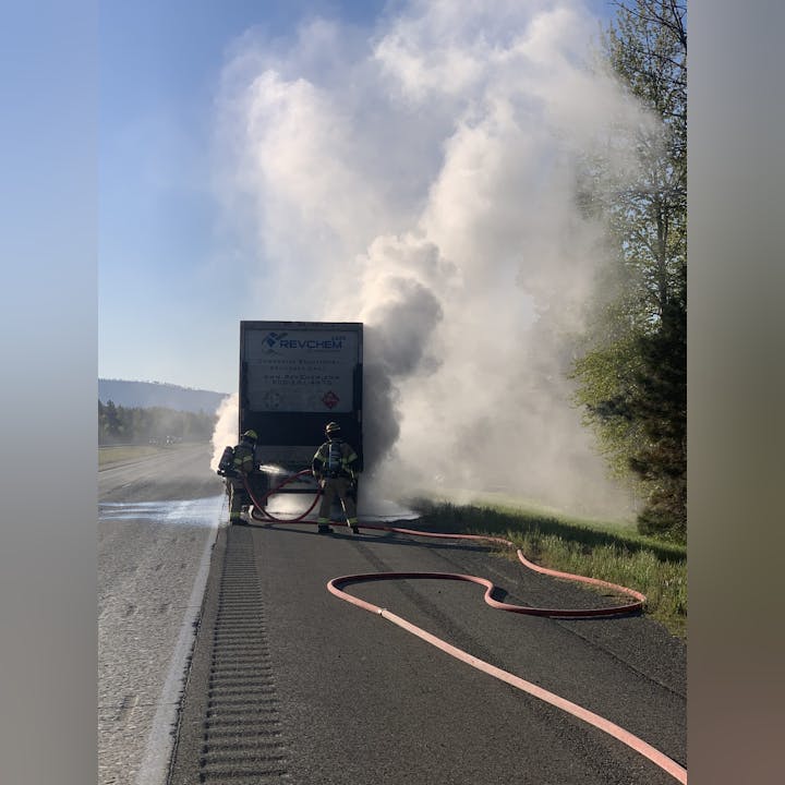 Firefighters extinguishing a smoking truck on the roadside with hoses.