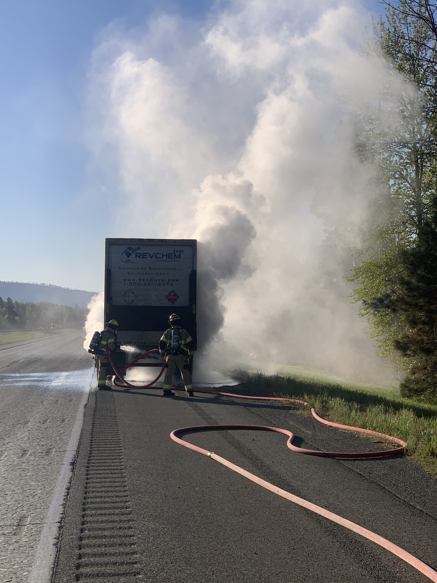 Firefighters extinguishing a smoking truck on the roadside with hoses.