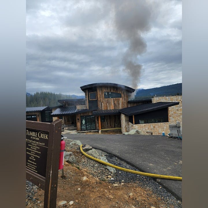 A wooden building with smoke rising, a sign for Tumble Creek, and construction materials are visible under a cloudy sky.