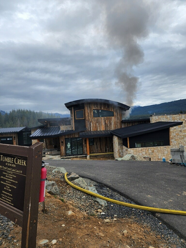 A wooden building with smoke rising, a sign for Tumble Creek, and construction materials are visible under a cloudy sky.