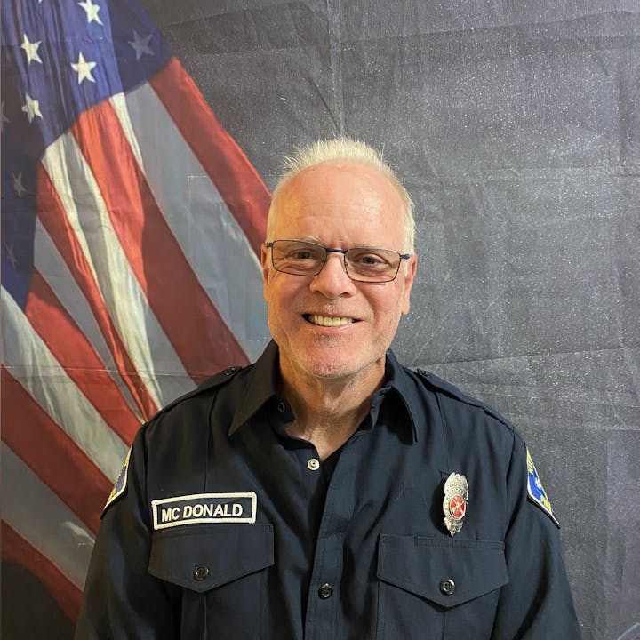 A man in a uniform with "MC DONALD" name tag, standing in front of an American flag.