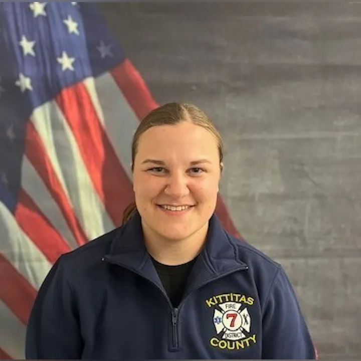 A person in a "Kittitas County Fire" jacket stands in front of an American flag.
