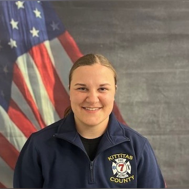 A person in a "Kittitas County Fire" jacket stands in front of an American flag.