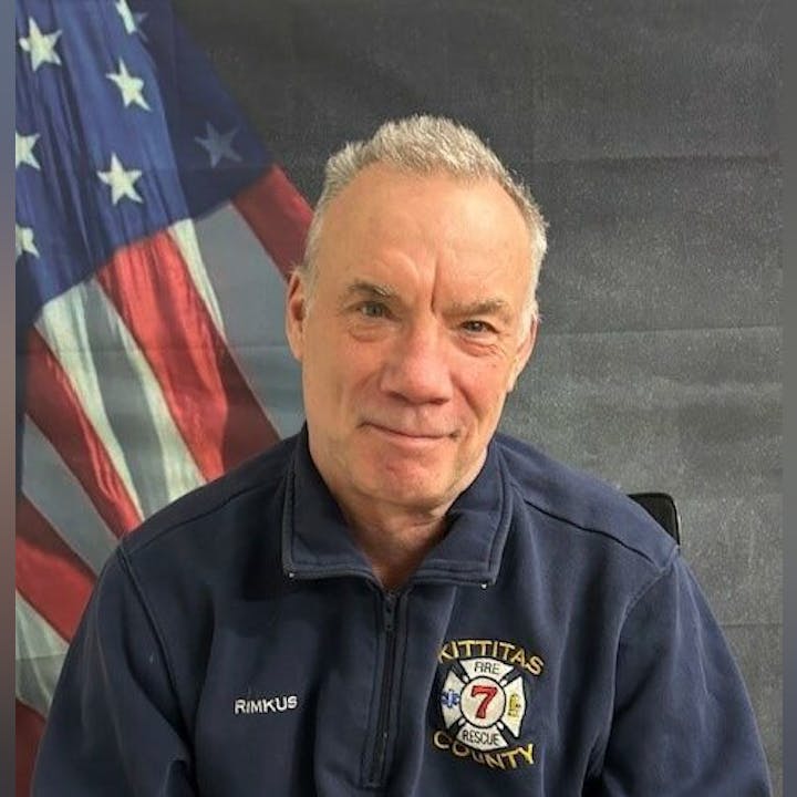 A person in a Kittitas County Fire & Rescue jacket with an American flag in the background.