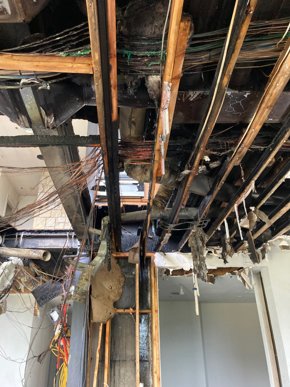Damaged ceiling with exposed wires and charred beams, showing structural and fire damage.