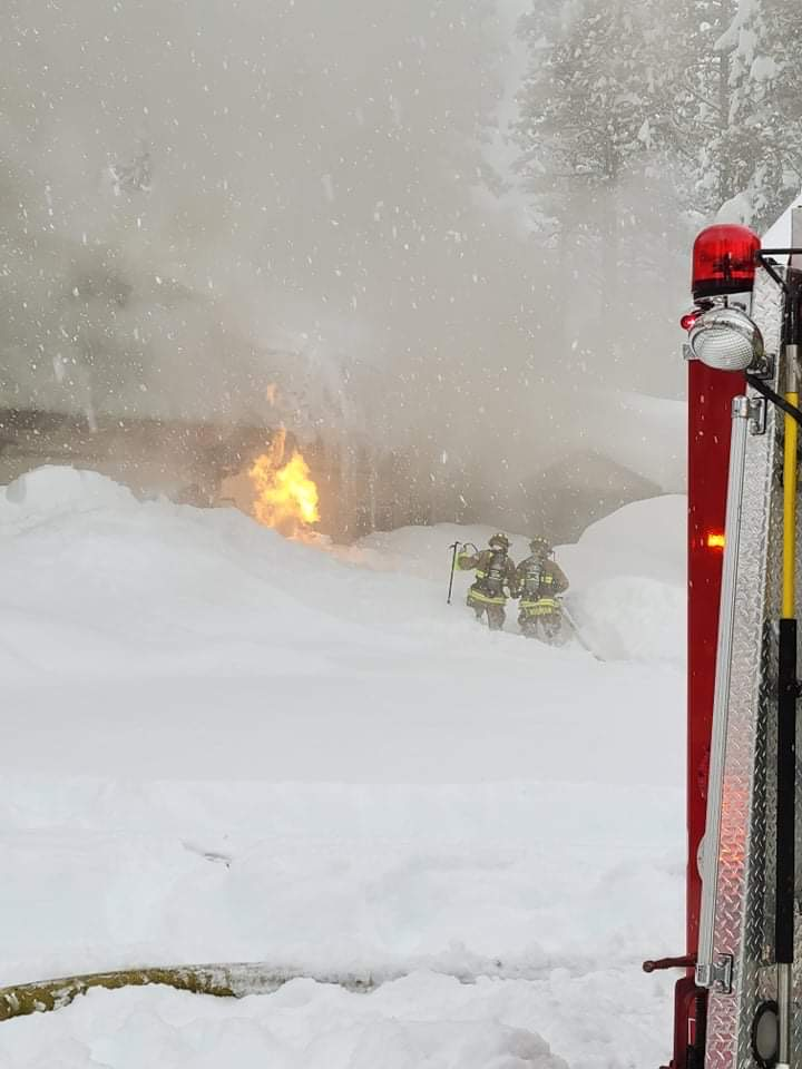 Firefighters battling a blaze in snowy conditions with smoke and flames visible. A fire truck is on the scene.