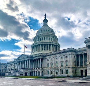 The image shows the U.S. Capitol building under a partly cloudy sky.