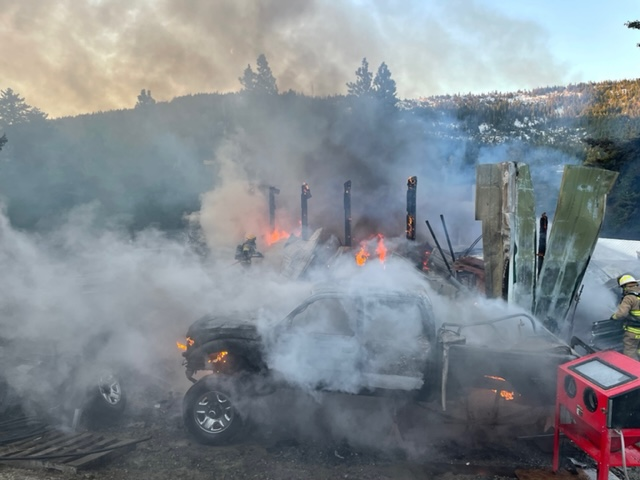 A burning structure with heavy smoke, visible flames, and firefighters attempting to extinguish the fire.