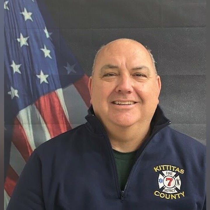 A person in a Kittitas County Fire District 7 jacket stands in front of an American flag.