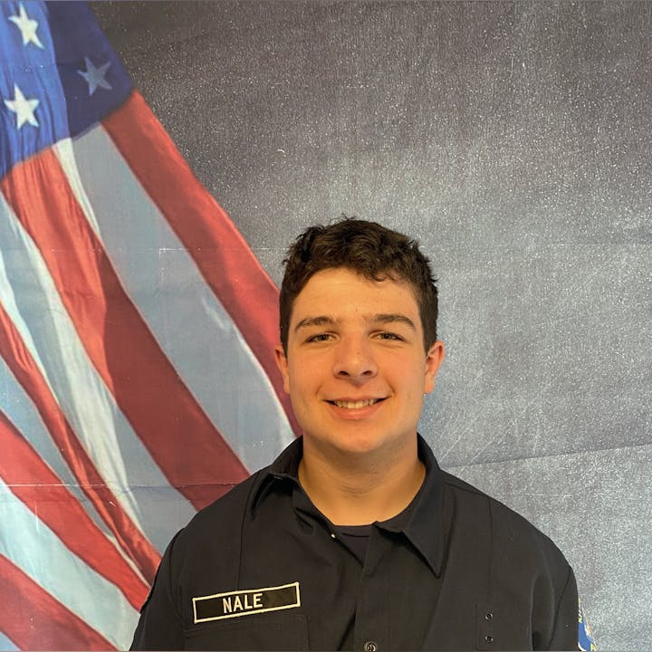 A person in a uniform standing in front of an American flag backdrop.