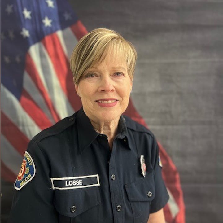 A person in a dark uniform poses in front of a U.S. flag backdrop.