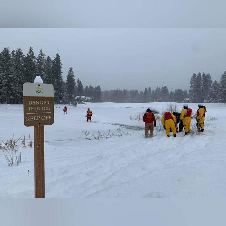 Sign warning of thin ice, people in rescue gear on snowy lake.