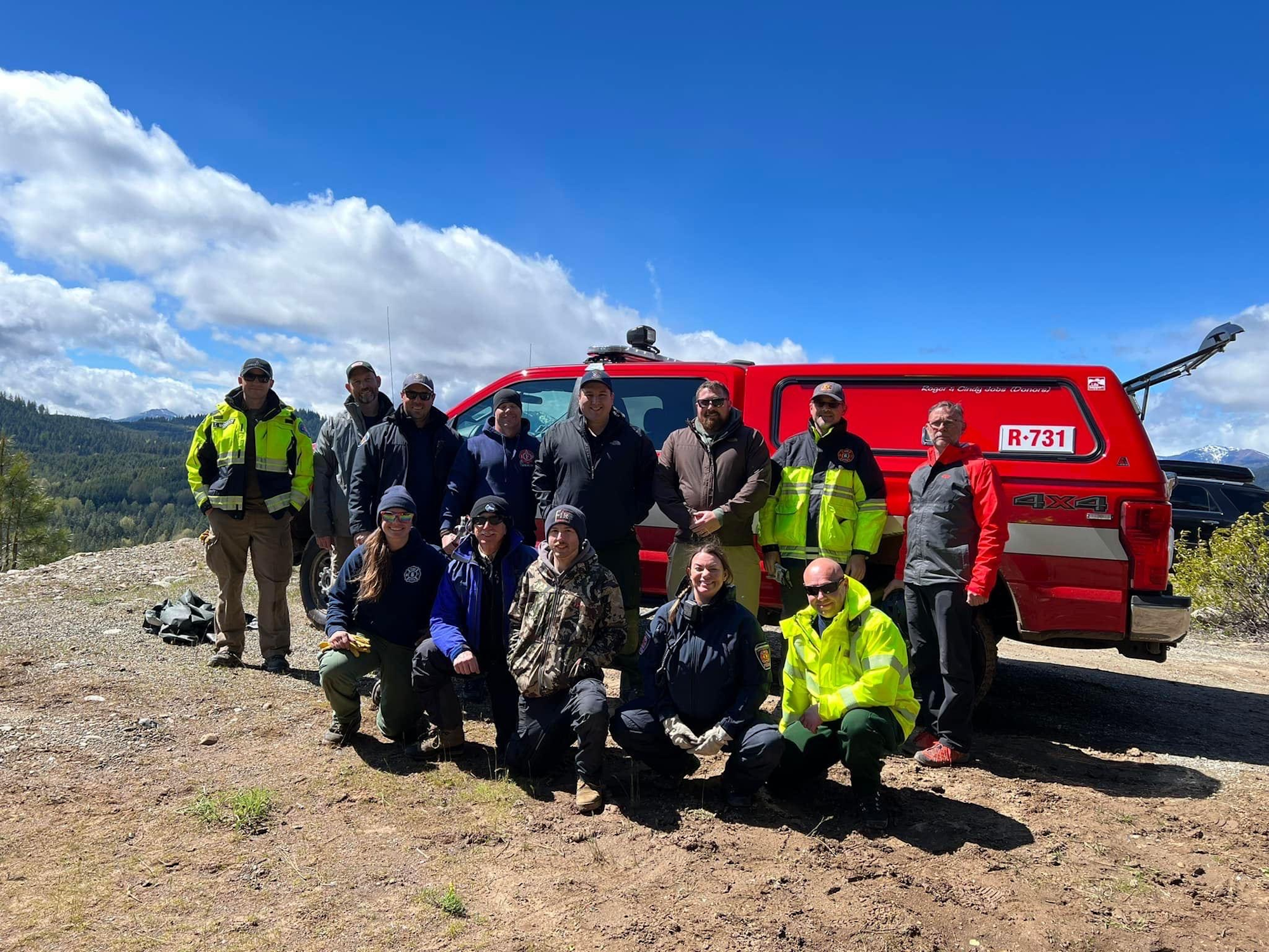 Group of people posing in front of a red rescue truck with a scenic mountain backdrop.