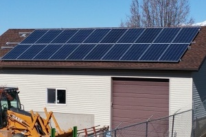 Solar panels on a garage roof with a clear sky above and construction equipment to the side.