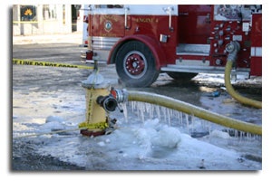 A frozen fire hydrant in the snow with a yellow hose attached to it