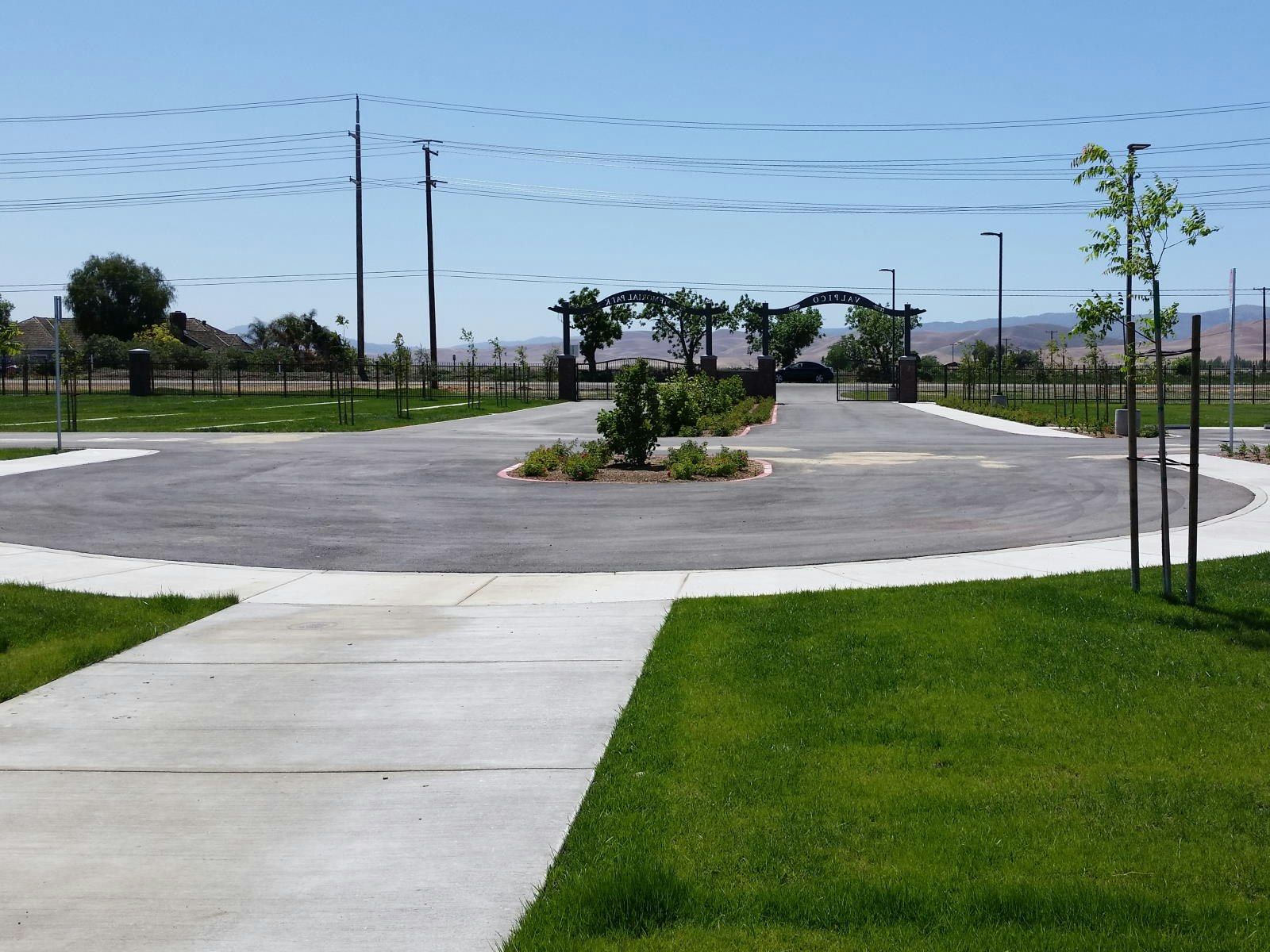 A circular driveway with landscaping, surrounded by grass, trees, and distant hills under a clear sky.