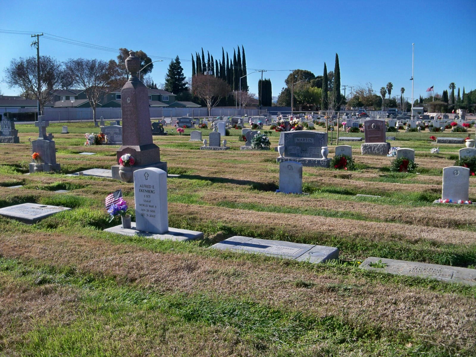 A cemetery with gravestones and flowers under a clear blue sky.
