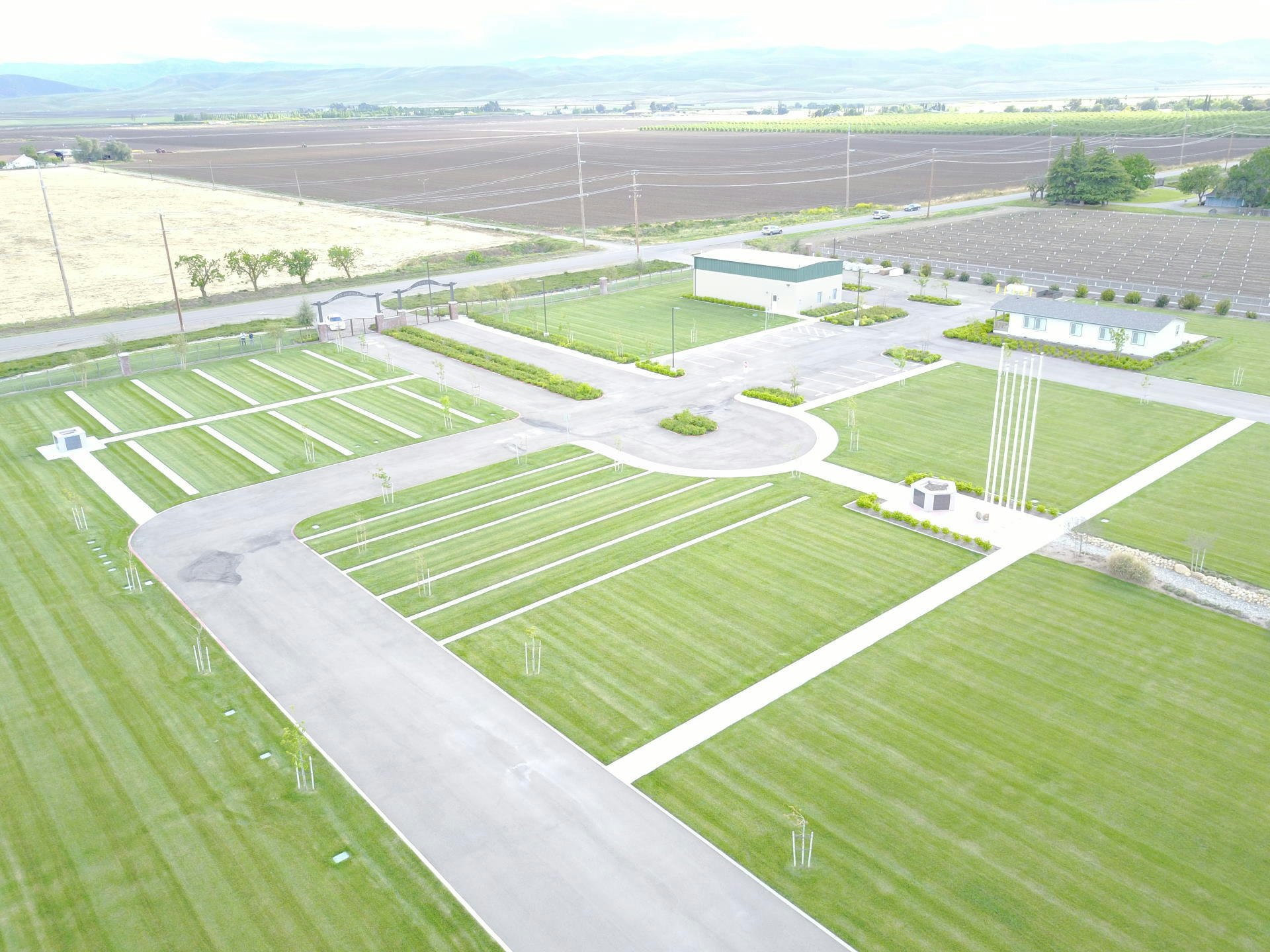 Aerial view of a landscaped area with roads, pathways, grassy sections, and a building, surrounded by agricultural fields.