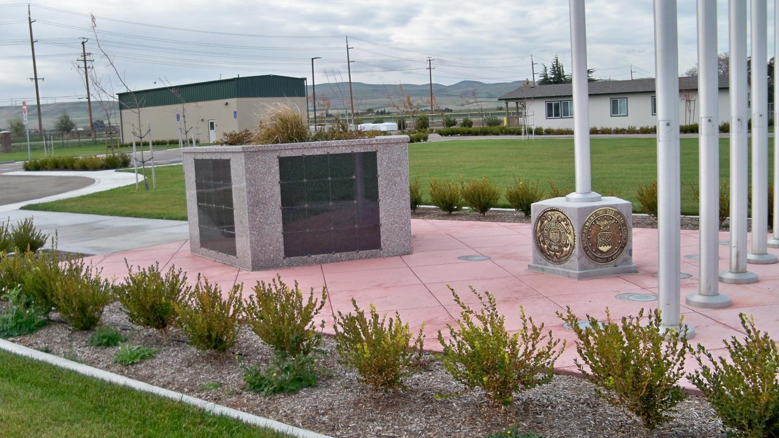 A granite memorial structure with engraved plaques and flagpoles in a landscaped area.
