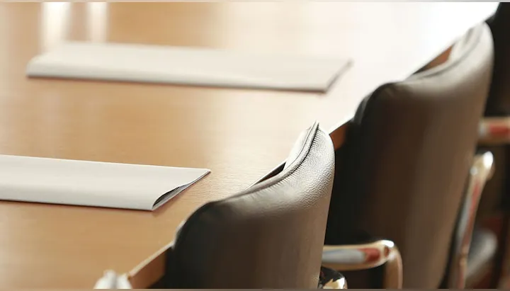 Conference room setup with a wooden table, white paper sheets, and leather chairs.