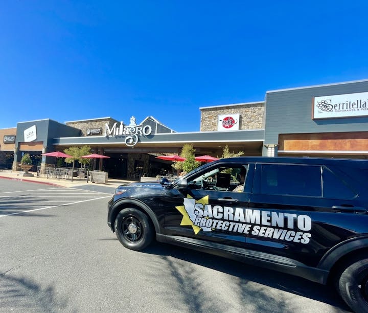 A Sacramento Protective Services vehicle parked in front of a shopping center with signs for Milagro, Taiko, and other businesses.