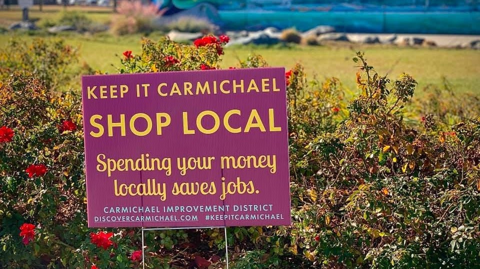 Sign urging to "Shop Local" in Carmichael, supporting jobs and economy.
