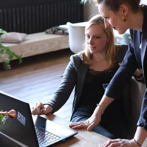 Two people are looking at a laptop screen in a workspace setting.