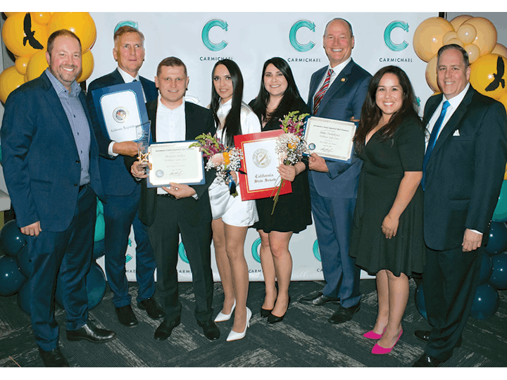 A group of people holding certificates and bouquets, posing for a photo in front of a backdrop with balloons.